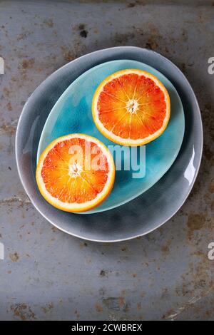 Fette di arancio di sangue siciliano su turchese brillante e piatti di ceramica grigia su fondo di metallo arrugginito. Disposizione piatta Foto Stock