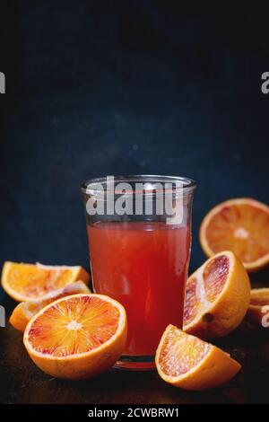 Fette di arance di sangue siciliano e un bicchiere di succo d'arancia rosso fresco sopra un vecchio tavolo di legno. Stile rustico scuro. Foto Stock