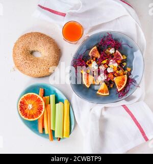 Piatto di insalata di frutta da carote colorate, formaggio blu, arance rosse e germogli di barbabietole, servito con succo di carota, bagel e verdure a fette Foto Stock