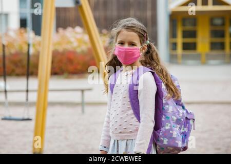 Studentessa indossando tessuto protettivo maschera riutilizzabile viso andare a scuola. Educazione scolastica durante la pandemia del coronavirus. Sicurezza, allontanamento sociale Foto Stock