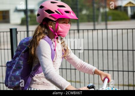 Studentessa indossa un tessuto protettivo maschera riutilizzabile che cavalca una bicicletta a scuola. Educazione scolastica durante la pandemia. Distanza sociale Foto Stock