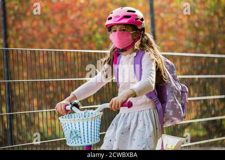 Studentessa indossa un tessuto protettivo maschera riutilizzabile che cavalca una bicicletta a scuola. Educazione scolastica durante la pandemia. Distanza sociale Foto Stock