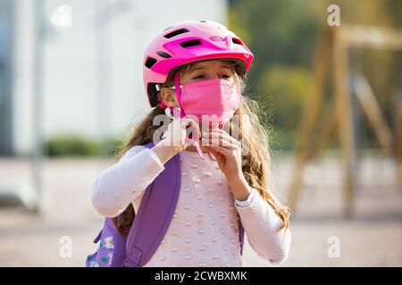 Studentessa indossa un tessuto protettivo maschera riutilizzabile che cavalca una bicicletta a scuola. Educazione scolastica durante la pandemia. Distanza sociale Foto Stock