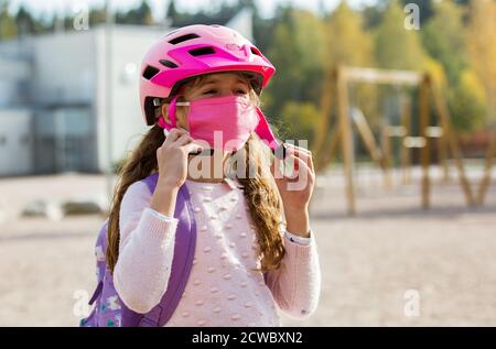 Studentessa indossa un tessuto protettivo maschera riutilizzabile che cavalca una bicicletta a scuola. Educazione scolastica durante la pandemia. Distanza sociale Foto Stock