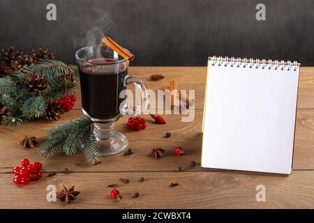 Taccuino aperto, rami di abete, bicchiere di VIN brulé, spezie e coni su sfondo di legno. Piani di scrittura per il nuovo anno. Nuovo concetto di inizio Foto Stock