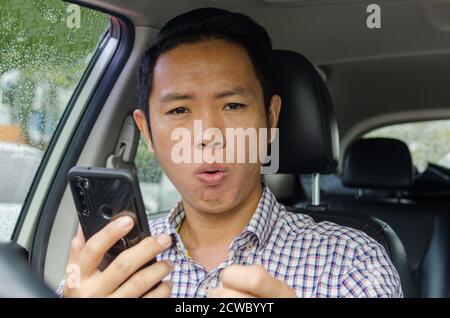 L'uomo asiatico che indossa una camicia a plaid guarda lo smartphone in un'auto. Foto Stock