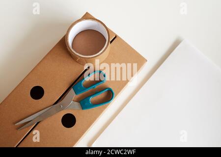 Vista ad angolo alto della scatola di cartone con nastro adesivo e. forbici su di esso isolate su sfondo bianco Foto Stock