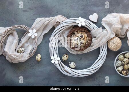 Appartamento di Pasqua con uova di quaglia in nido d'uccello con tessuto di lino. Fiori di legno e corona di rattan, decorazione primaverile. Foto Stock