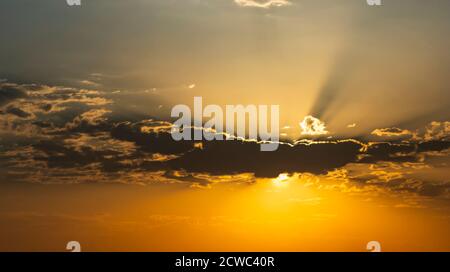 Il sole si nasconde dietro uno strato di nuvole all'alba, solo i suoi raggi che escono. Foto Stock