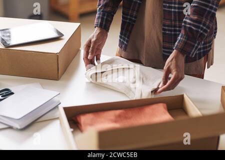 Primo piano di un uomo che impacchetterà nuovi abiti nella scatola di cartone al tavolo Foto Stock