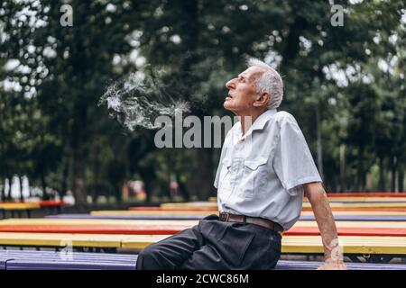 Gli uomini anziani fumano sigarette all'aperto nel parco cittadino quando si è seduti sul banco Foto Stock