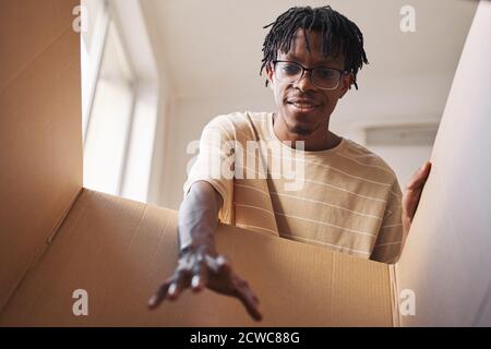 Giovane africano che stende la mano e togli fuori il pacco dalla scatola Foto Stock