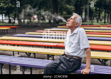 Gli uomini anziani fumano sigarette all'aperto nel parco cittadino quando si è seduti sul banco Foto Stock