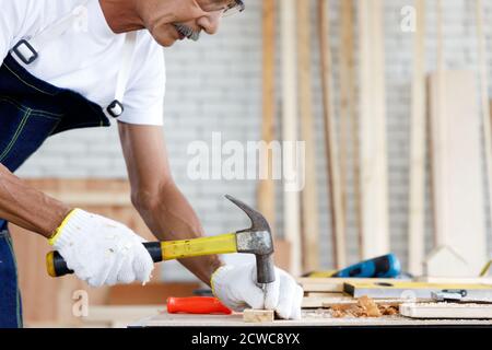 Uomo anziano unghia legno asse in Falegnameria officina. Concetto di persone anziane che fanno hobby dopo il pensionamento. Foto Stock