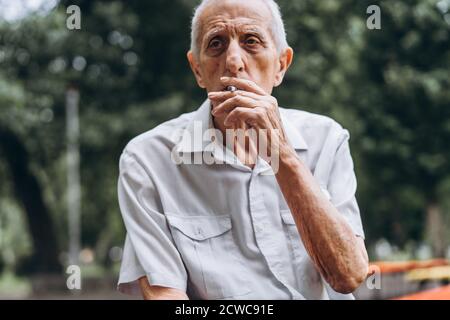 Gli uomini anziani fumano sigarette all'aperto nel parco cittadino quando si è seduti sul banco Foto Stock