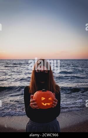 Donna che indossa una maschera protettiva che tiene jack o lanterna zucca Foto Stock