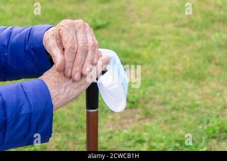 Vecchia signora che tiene il bastone da passeggio su fondo erba. Primo piano delle mani anziane che poggiano sul bastone nel parcheggio. Donna anziana che tiene il bastone da passeggio. Mani senior Foto Stock