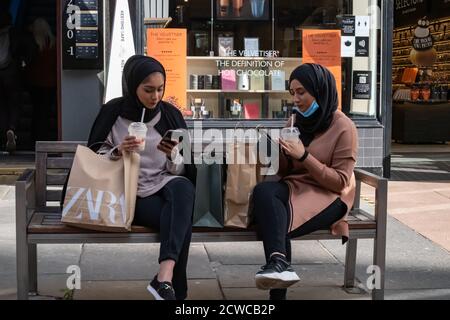 Glasgow, Scozia, Regno Unito. 29 Settembre 2020. Regno Unito Meteo. Due ragazze con le borse della spesa seduti su una panchina sia usando il loro telefono cellulare che tenendo una bevanda di Tim Hortons in via Buchanan. Credito: SKULLY/Alamy Live News Foto Stock