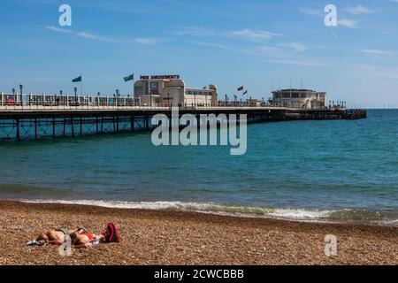 Inghilterra, West Sussex, Worthing, Worthing Beach, coppia prendere il sole sulla spiaggia con Pier in background Foto Stock