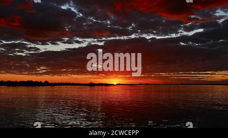 Incredibile tramonto multicolore con cielo rosso e arancione e nuvole che si riflettono in acqua sul fiume Chobe durante il safari in barca, il parco nazionale di Chobe, il Botswana. Foto Stock