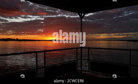 Incredibile tramonto colorato con cielo rosso e arancione che si riflette in acqua, girato da barca safari sul fiume Chobe vicino Kasane, Chobe Riverfront, Botswana. Foto Stock