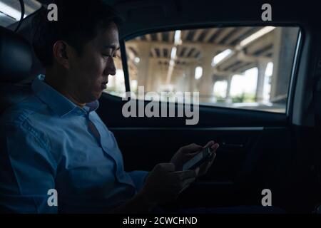 Uomo d'affari allegro seduto sul sedile posteriore dell'auto che chiacchiera al telefono, in movimento, viaggio d'affari, comunicazione, fiducia Foto Stock