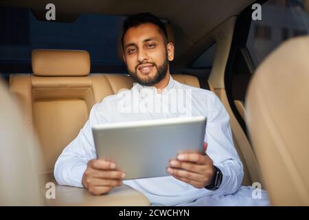 Ritratto di giovane uomo bearded che sorride alla macchina fotografica durante l'uso tablet digitale in auto Foto Stock