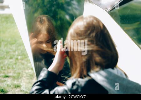 bella ragazza che guarda nella superficie dello specchio outdoorsona giorno di sole Foto Stock