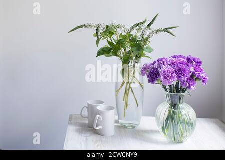 Bouquet nuziale di garofani lilla in quattro vasi rotondi di vetro di diverse dimensioni come decorazione della tavola. Due tazze bianche. Foto Stock