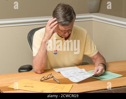 Uomo caucasico anziano seduto alla scrivania di casa e completando il scrutinio per posta o assenti per le elezioni presidenziali del 2020 Foto Stock