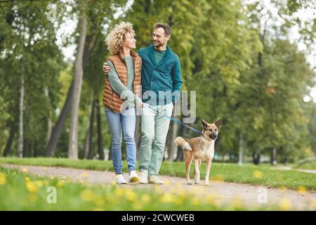 Giovane coppia che cammina con il cane insieme nel parco all'aperto Foto Stock