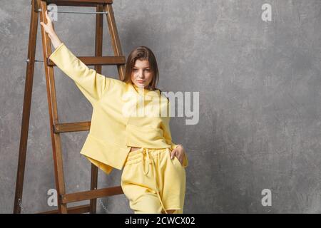 Giovane donna con abbigliamento sportivo giallo, pantaloni e felpa. Concetto di outfit sportivo alla moda, foto in interni. Spazio di copia. Foto Stock