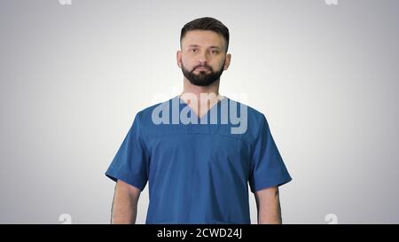 Chirurgo maschile serio con una barba che cammina su sfondo gradiente Foto Stock