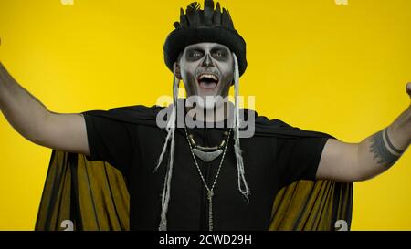 Uomo creepy con trucco scheletro in top-Hat. Felice ragazzo che celebra la vittoria, emotivamente gioendo in vittoria successo, vincitore, gridando di sì. Festa tematica di Halloween. Sfondo giallo Foto Stock