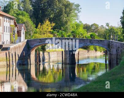 Antico ponte in pietra che si riflette nelle acque del canale navigabile del Parco Ticino vicino a Milano in una giornata di sole. Foto Stock