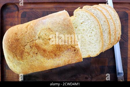 Angolo di testa, pane fresco fatto in casa, affettato, su tagliere scuro, con coltello verso il lato. Foto Stock