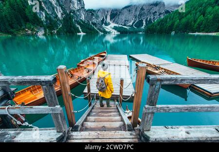 Storie di montagna. Felice zaino in spalla in una vacanza wanderlust. Uomo con un impermeabile giallo in piedi di fronte al lago e godere della vista Foto Stock