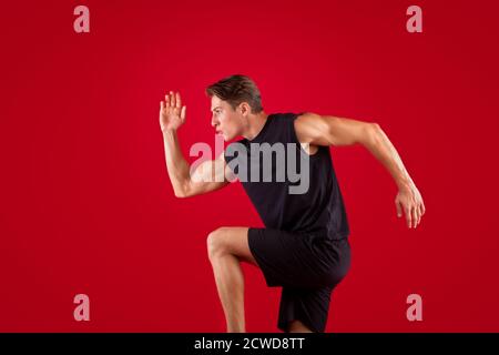 Ritratto di un giovane uomo concentrato che corre velocemente in studio rosso sfondo Foto Stock