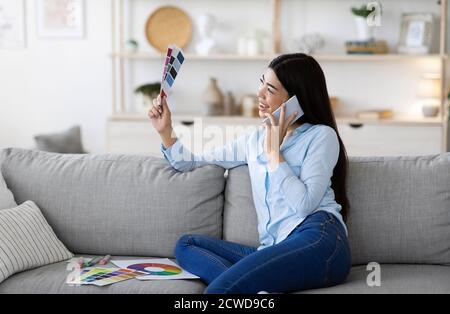 Donna coreana che sceglie Interior Design, Holding Color palette e parlando su Cellphone Foto Stock