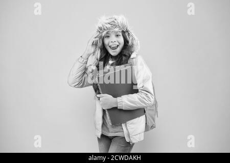 Sentire lo spirito. inverno vacanze e vacanze. kid vestiti caldi sfondo rosa. allievo vita quotidiana. schoolgirl zaino e libri vai home. non più esami. piccola ragazza felice earflap hat. torna a scuola. Foto Stock