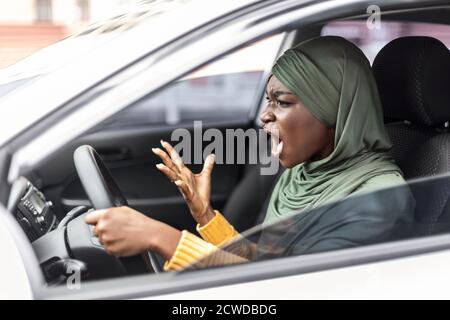 Stress del traffico. Arrabbiato nero musulmano donna guida auto e gridare a qualcuno Foto Stock