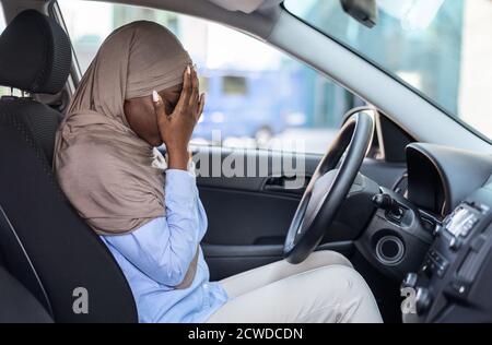 Stressato driver nero musulmano seduto in auto, coprendo il viso con le mani Foto Stock
