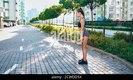 Giovane donna muscolare allenamento gambe, esercizio controllato esercizi con elastico fitness corda fascia. Vista laterale di affascinante ragazza che fa deadlift utilizzando la banda di resistenza in sole mattina all'aperto. Foto Stock