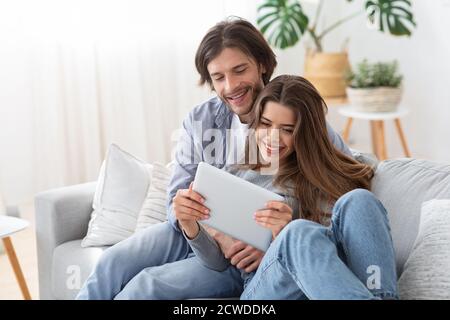 Una giovane coppia positiva innamorata dell'uso del tablet digitale a casa Foto Stock