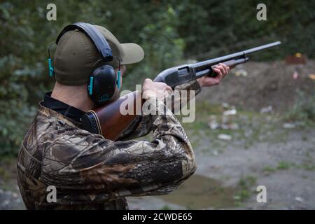 Un uomo vestito in camo sta puntando un vecchio downrange di fucili da calcio in legno pronto a tirare il grilletto. Foto Stock