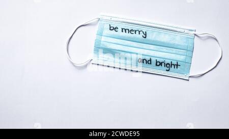 Una maschera medica con scritto 'Be Merry e Bright' La maschera per il Natale e le vacanze durante la corona Pandemia virale Foto Stock