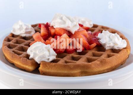 Generoso pasto servito con un sostanzioso waffle alla fragola decorato con panna montata su piatto rotondo. Foto Stock