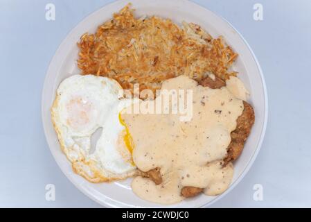 Vista dall'alto di un abbondante pasto che serve una sostanziosa bistecca di pollo fritta, uova e crocchette di patate che sgocciolano con sugo di carne. Foto Stock