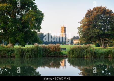 La Chiesa di San Giovanni Battista dai terreni abbaziali che si riflette nel lago abbaziale all'alba. Cirencester, Cotswolds, Gloucestershire, Inghilterra Foto Stock