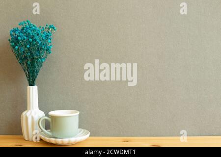 Tazza da caffè con vaso di gypsophila secco con alito del bambino blu fiori su tavolo di legno con sfondo grigio Foto Stock